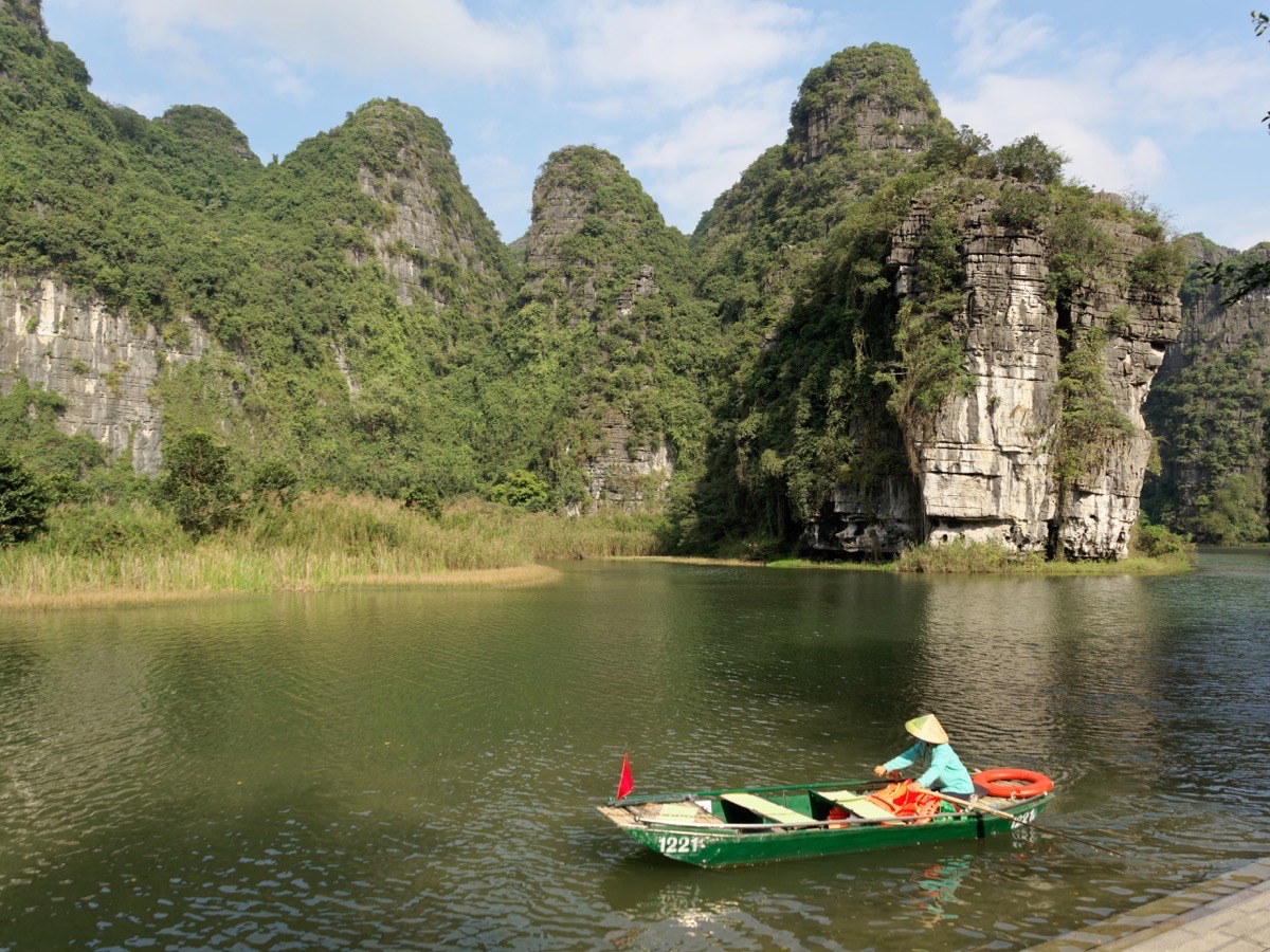A small boat on the river beneath limestone cliffs at Trang An